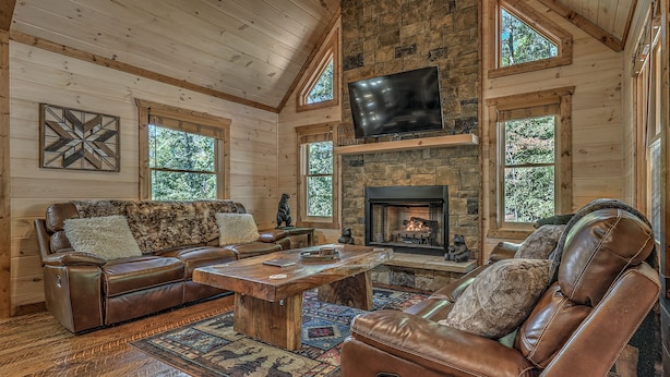 A cozy living room with a stone fireplace, leather furniture, and large windows. - Raven’s Retreat: Sauna, Putting Green & Arcade! (Blue Ridge)