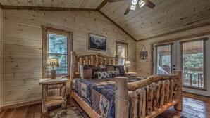 A log cabin bedroom with a wooden bed, a ceiling fan, and large windows. - Raven’s Retreat: Sauna, Putting Green & Arcade! (Blue Ridge)