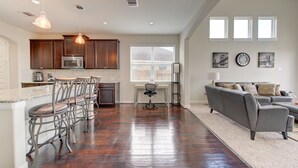 A spacious living area with a gray sofa, a kitchen with dark wooden cabinets, and a dining area with bar stools. - 5-STARS HOST! Spacious 4-2.5 Pearland Clear Lake Friendswood. World Cup 2026 (Houston)