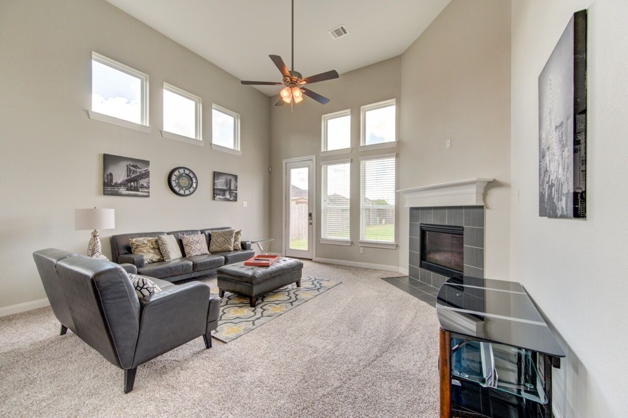 A spacious living room with a fireplace, a ceiling fan, and large windows.