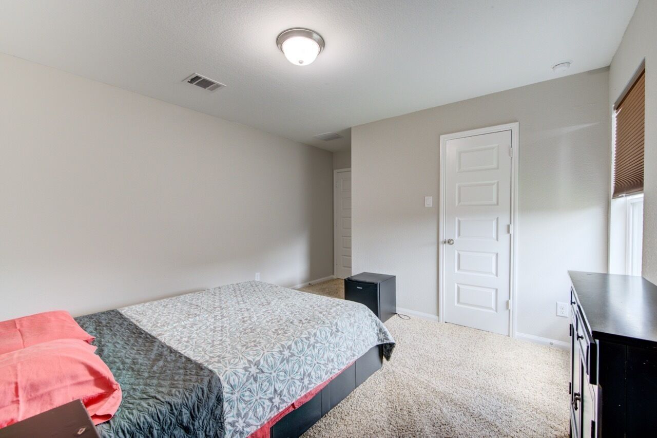 Ein Schlafzimmer mit Bett, Kommode, Tür und Deckenleuchte.