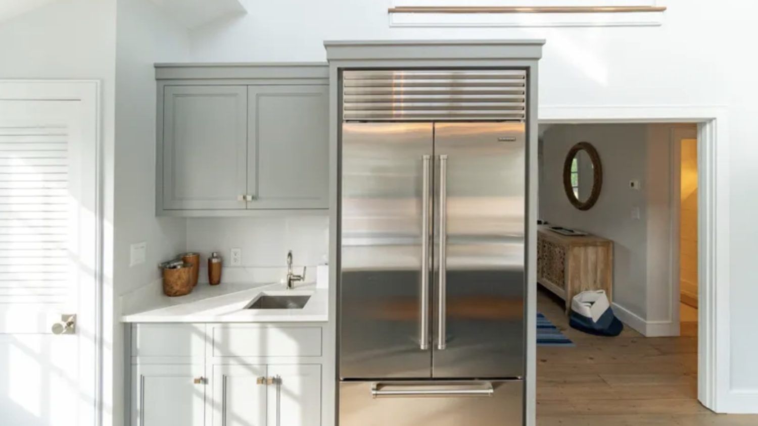 A modern kitchen with a stainless steel refrigerator, white cabinetry, and a built-in oven.