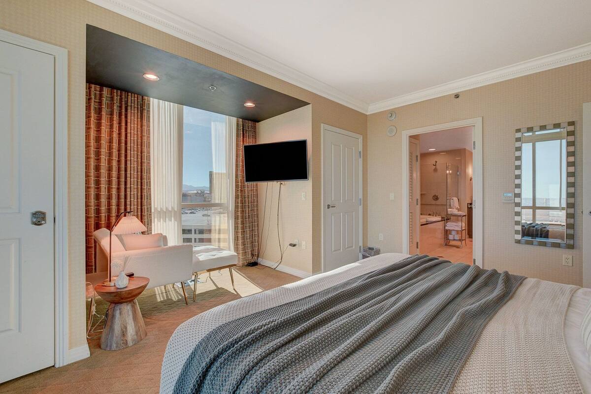 Une chambre d’hôtel dotée d’un grand lit, d’un coin salon avec une table et des chaises, d’un téléviseur fixé au mur et d’une salle de bain visible à travers une porte ouverte.