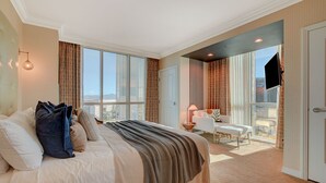 Ett rymligt hotellrum med en stor säng, en sittgrupp med en fåtölj och ett bord samt en balkong med en tv.