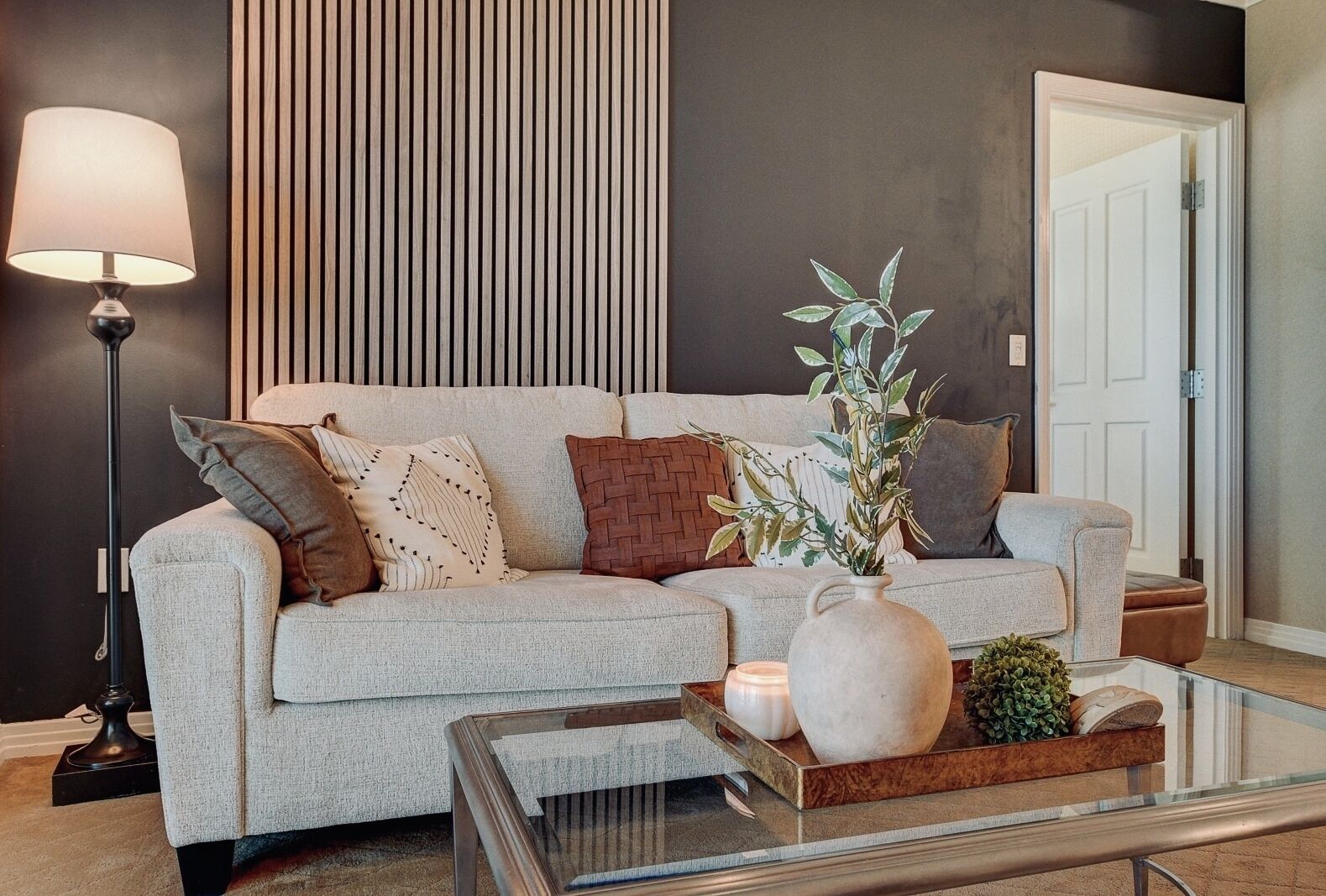 Un salon avec un canapé, une lampe sur pied, un vase avec des plantes et un plateau avec des bougies.