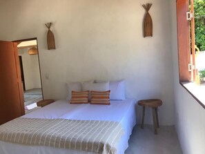 A bedroom with a bed, pillows, a bedside table, a mirror, and a window.