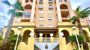 Een meerlaags hotel met een centrale trap, balkons en palmbomen.