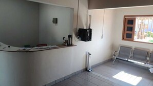 A reception area with a curved desk, a coffee machine, a trash bin, and a window with a view of the outside. - Pousada Paraiso (Wanderley)