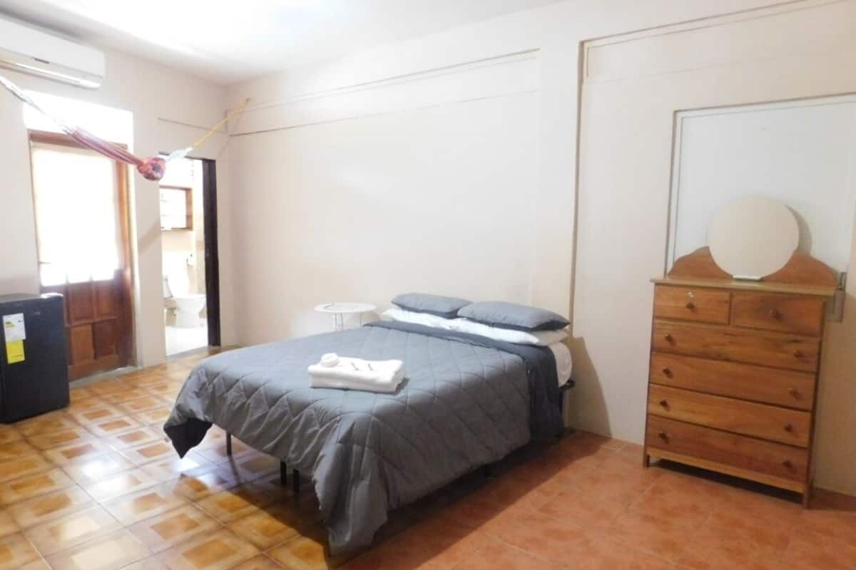 A bedroom with a bed, a dresser, a small table, and a door.
