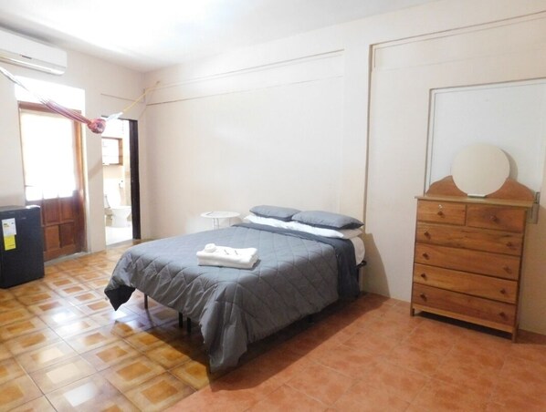 Un dormitorio con una cama, un aparador, una mesita y una puerta.