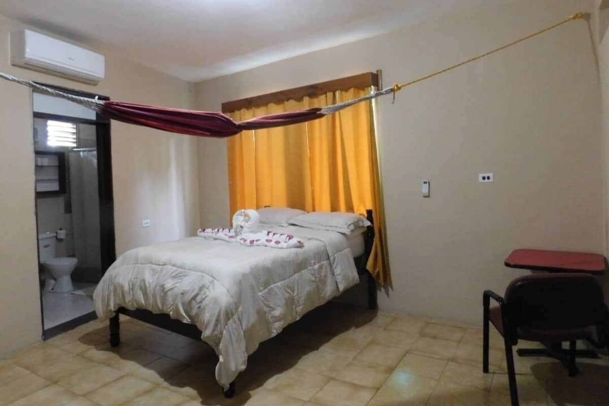 A small, single-bed room with a curtain, a chair, and a small table.