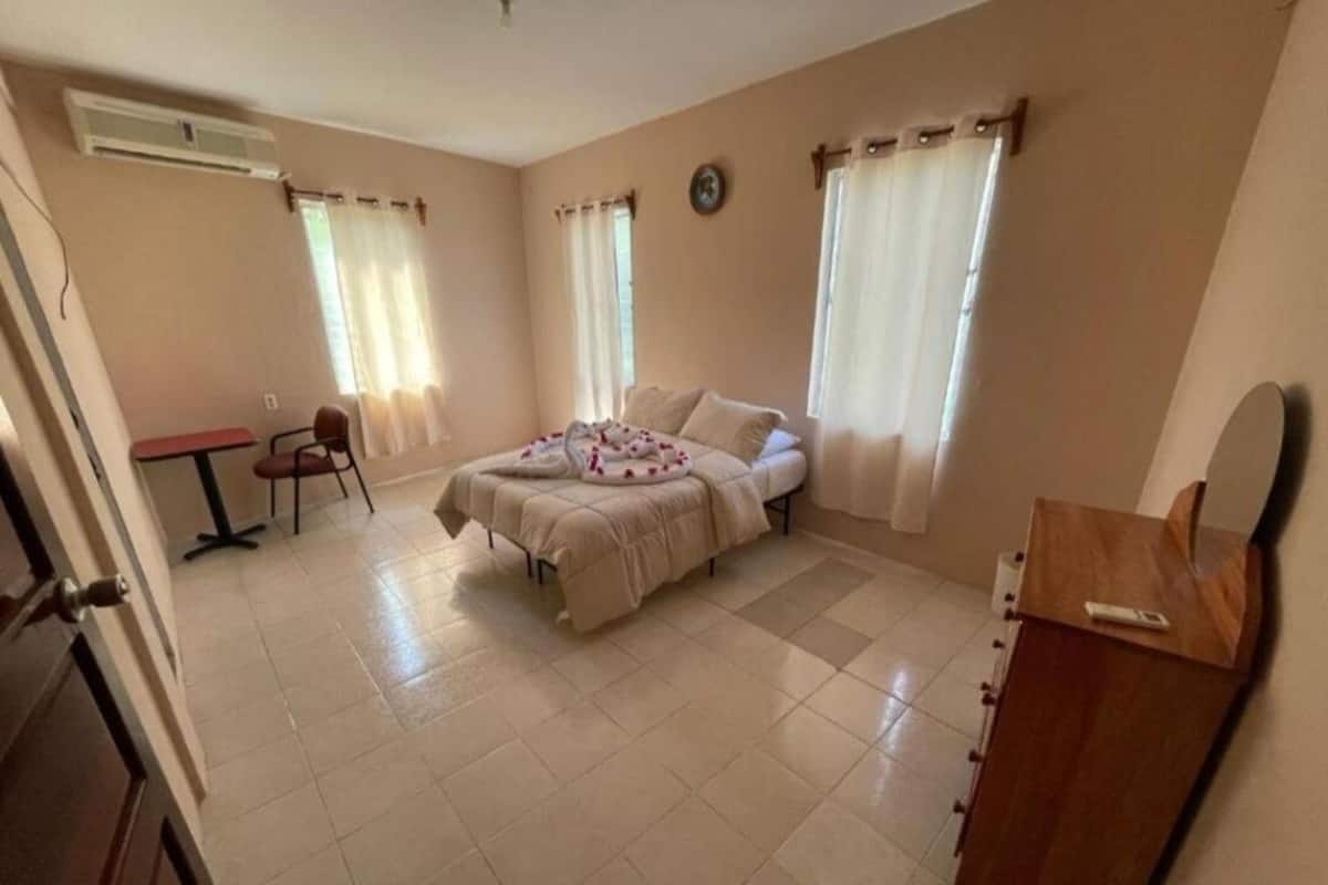 A bedroom with a bed, a desk, and a chair. There is a clock on the wall and a window with curtains.