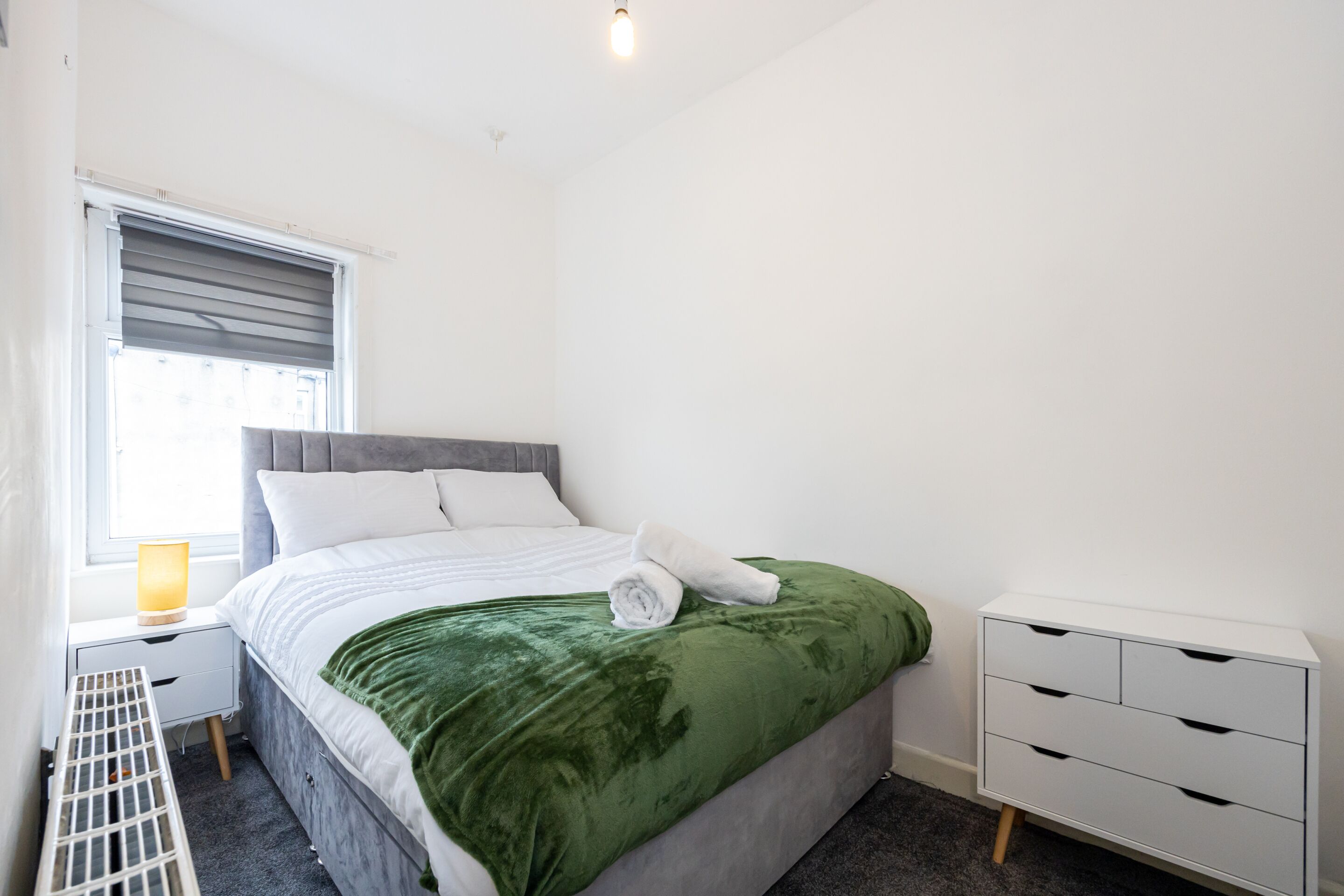 Une chambre à coucher bien rangée, avec un lit, une table de chevet, une lampe et une commode.