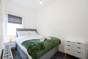 Un dormitori ben organitzat amb un llit, una taula de nit, una làmpada i un armari.