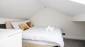 Un dormitorio con cama, almohadas, una mesita de noche y un enchufe.