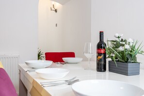 A dining table set with white plates, bowls, and cutlery, a wine bottle, and a potted plant with white flowers.