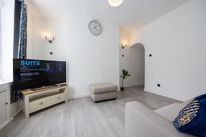 A modern living room with a flat-screen TV, a sofa, a small ottoman, a potted plant, and a wall-mounted clock. - Manor Terrace Retreat Accrington (Accrington)