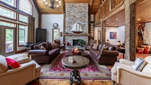 A spacious living room with leather sofas, a stone fireplace, and large windows. - 8 bed 5 bath cottage on Lake Muskoka, 9 acres! (Torrance)