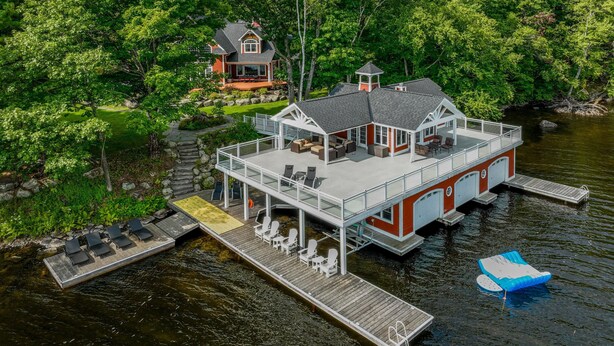 A large house with a dock extending into a lake, surrounded by lush greenery. - 8 bed 5 bath cottage on Lake Muskoka, 9 acres! (Torrance)