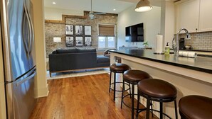 A modern kitchen with a stainless steel refrigerator, a black countertop, and a bar area with stools.