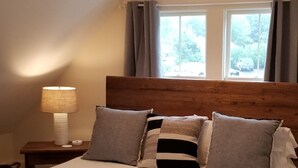 A bedroom with a large bed, two bedside lamps, a wooden headboard, a window with curtains, and a small bench. - King Suite at Public House, food trucks & craft beer on site, walk to UNH & town (Durham)