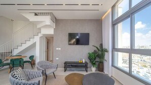 Una sala de estar moderna con una escalera, un televisor de pantalla plana montado en la pared y ventanas amplias con vistas a la ciudad.