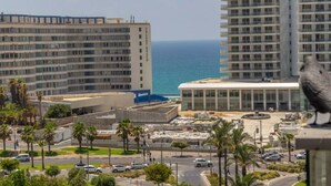 Un paisaje urbano costero con edificios altos, un edificio moderno con fachada de vidrio y una estatua de un ave.