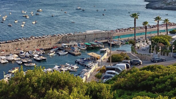A coastal marina with boats docked, a promenade with palm trees, and a hilly landscape in the background. - Apartment with sea-view balcony from which to admire magical sunrises. (Castro)