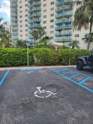 Un área de estacionamiento con un espacio reservado para discapacitados, una línea azul delimitándolo y un edificio con varios balcones al fondo.