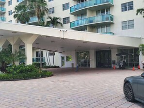 Un edificio moderno con acceso cubierto, palmeras y un cartel de servicio de valet.
