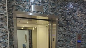 An elevator with a digital display, a metallic door, and a wall with a mosaic pattern.