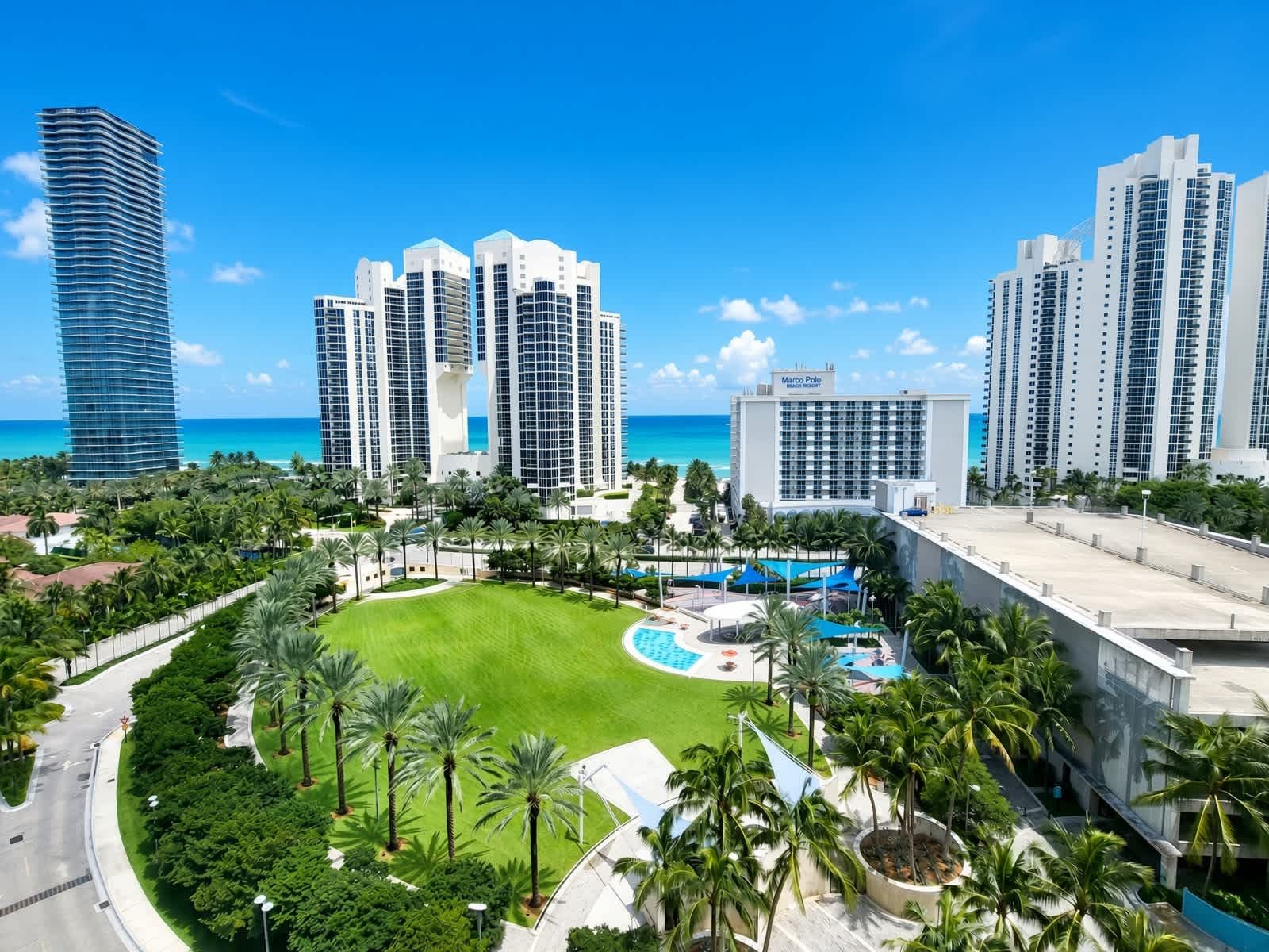 A high-rise hotel complex with multiple buildings, a swimming pool, and a well-maintained lawn.