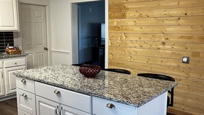 Une cuisine avec des meubles blancs, un plan de travail en granit et un mur en bois.