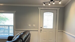 Une pièce avec un canapé en cuir, un plancher en bois, une porte blanche avec une fenêtre et un luminaire au plafond.