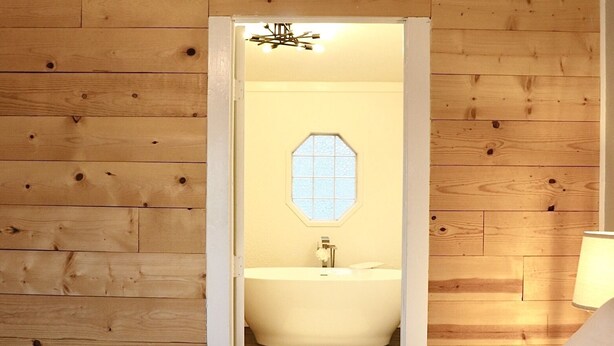 Une chambre avec un mur en bois, un lit blanc et une salle de bain visible à travers une porte ouverte.