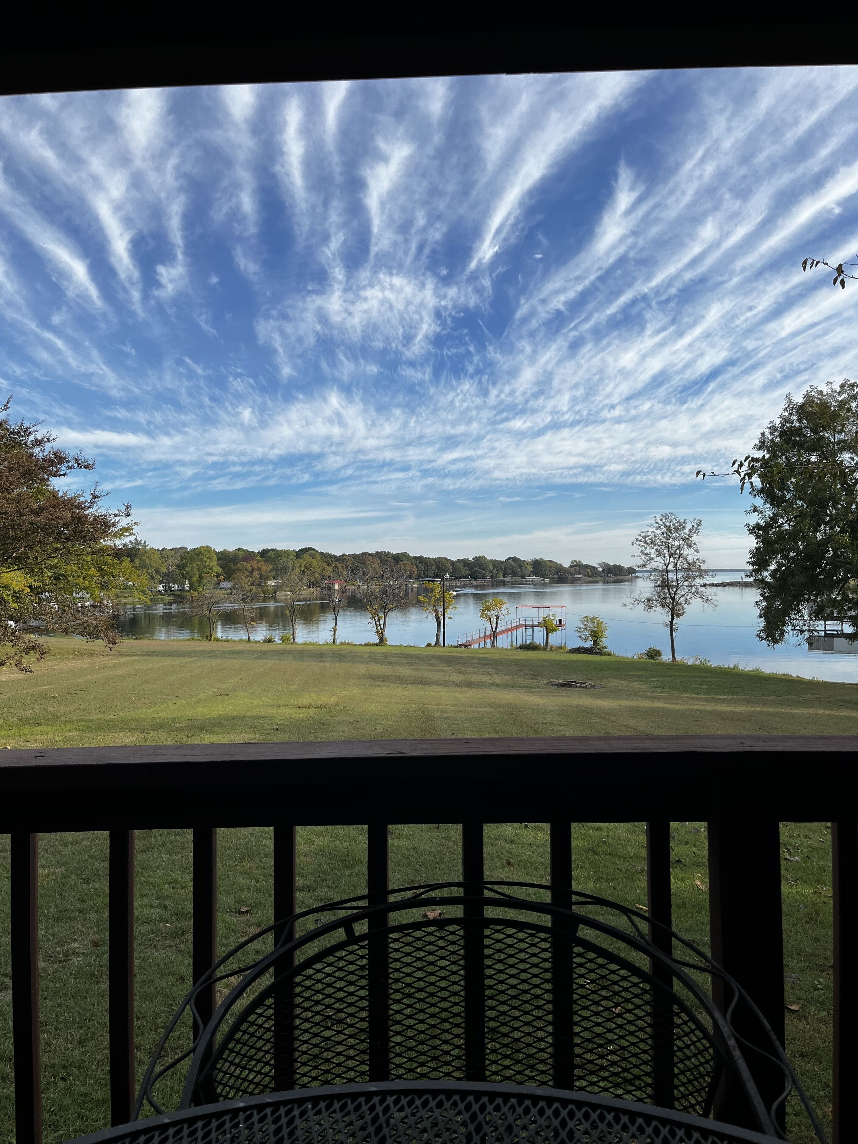 Une vue depuis un balcon donnant sur un lac, avec un ciel dégagé et des arbres qui se dessinent à l’horizon.