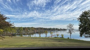 Une vue depuis un balcon donnant sur un lac, avec un ciel dégagé et des arbres qui se dessinent à l’horizon.