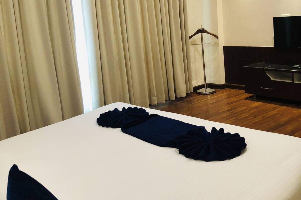 A hotel room with a neatly made bed, a television on the wall, and a floor lamp.
