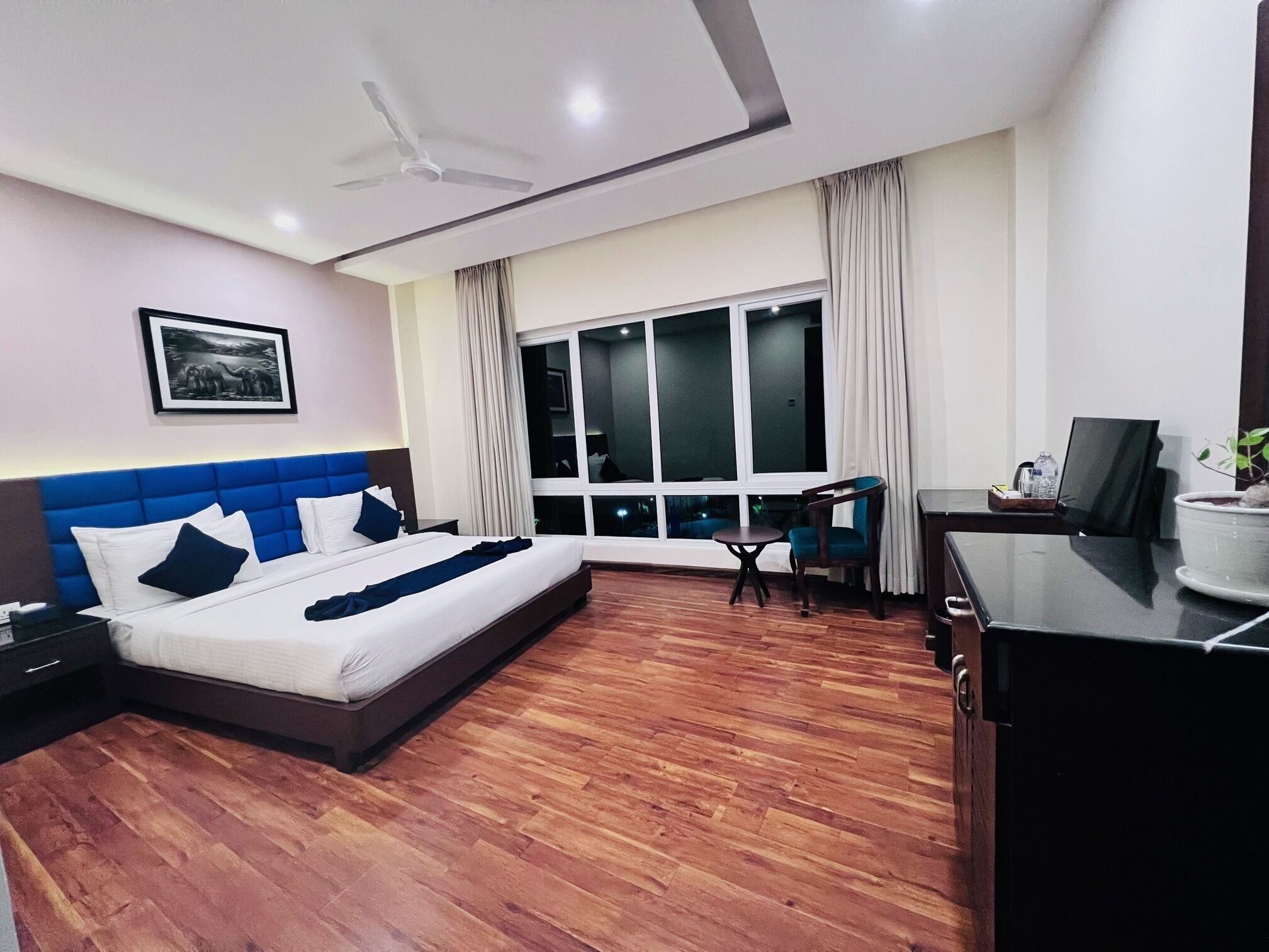 A modern hotel room with a large bed, a desk, a chair, and a TV.