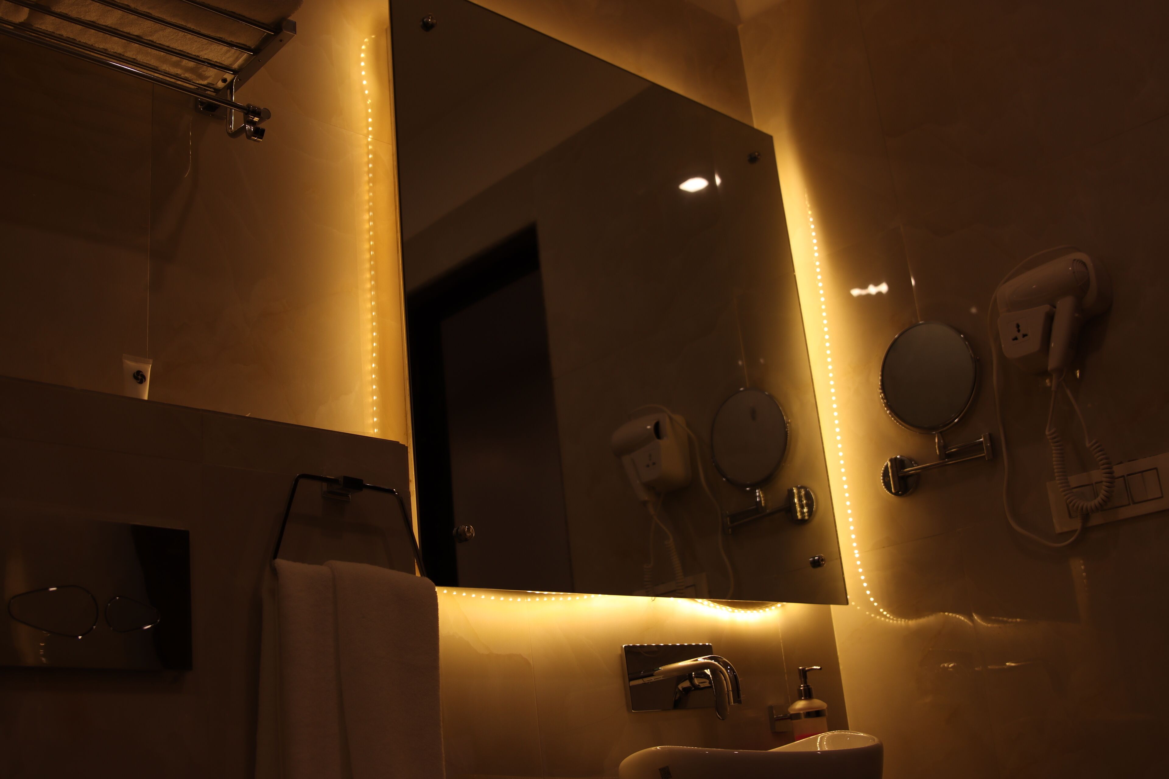 Une salle de bain avec un grand miroir, un porte-serviettes, un lavabo et un sèche-cheveux.
