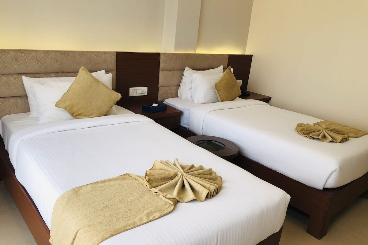 Two twin beds with white linens and beige throw pillows, a bedside table with a tissue box, and a round clock.