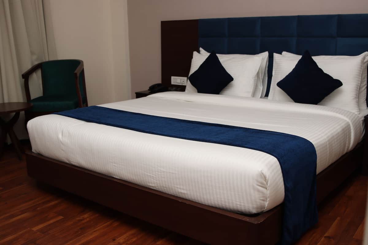 A hotel room with a large bed, a wooden headboard, a green chair, and a nightstand with a phone.