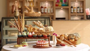 A display of pastries and bread on a table with a glass case in the background. - Nepalirika Hotel Biratchowk (Sundar Haraicha)