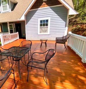 Una terraza de madera con sillas y una mesa de metal, una casa con techo a dos aguas y una barandilla blanca.