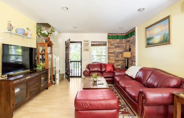 Una sala de estar con un sofá de cuero rojo, un mueble de madera con un televisor y una pared de piedra.