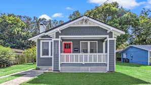 A single-story house with a grey exterior, a red door, and a white porch. - Fancy Dancy (Jacksonville)