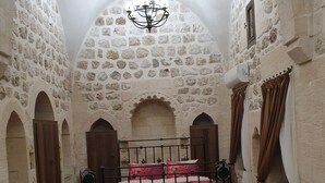A room with a stone wall, a bed with a metal frame, and green upholstered chairs. - Kale Divan Konağı (Mardin)