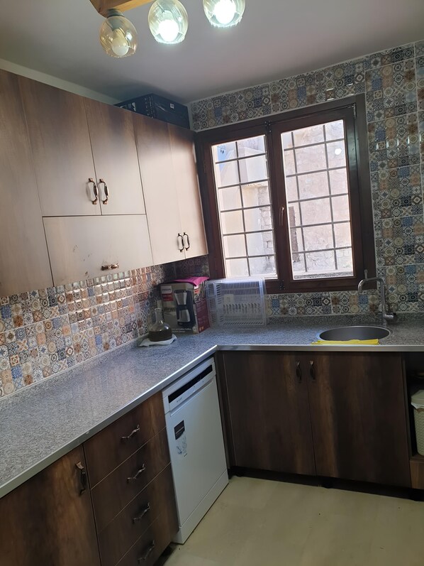 Una cocina con salpicadero de azulejos estampados, armarios de madera, lavavajillas integrado y una ventana con vistas al exterior.