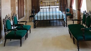 A room with a stone wall, a bed with a metal frame, and green upholstered chairs. - Kale Divan Konağı (Mardin)