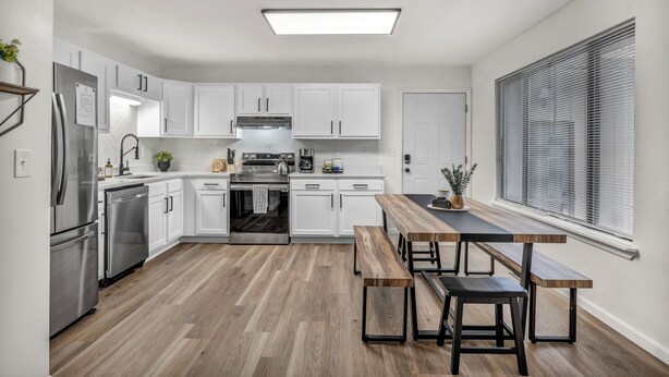 A modern kitchen with white cabinets, stainless steel appliances, and a wooden dining table with benches.